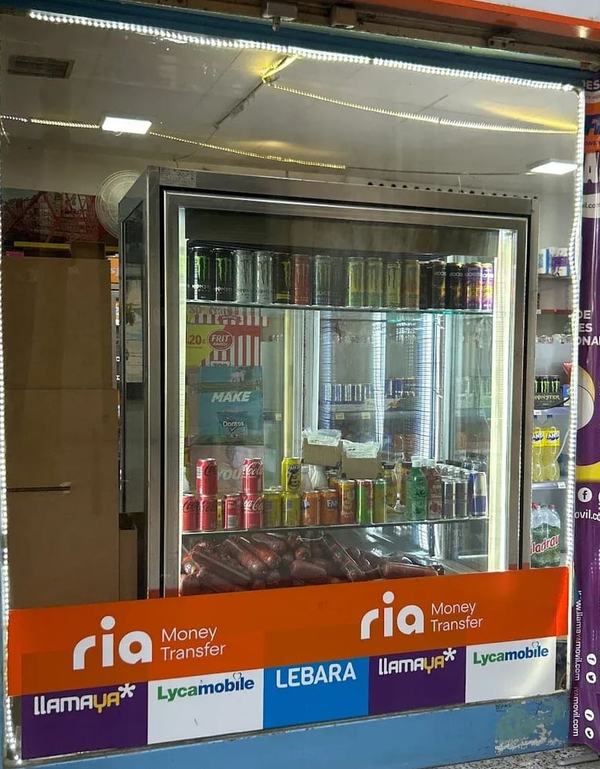 La nevera de bebidas de Tienda Ouassim vista desde el escaparate, con latas de refrescos y bebidas energéticas