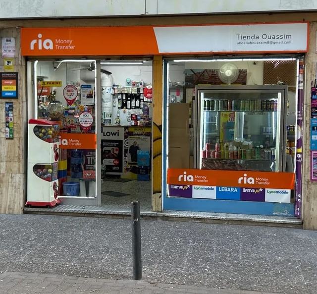 La entrada de Tienda Ouassim: rótulo naranja de Ria, la puerta abierta y el letrero blanco con el nombre de la tienda